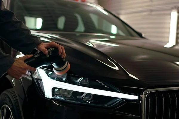 Detailer polishing the headlight of a black car